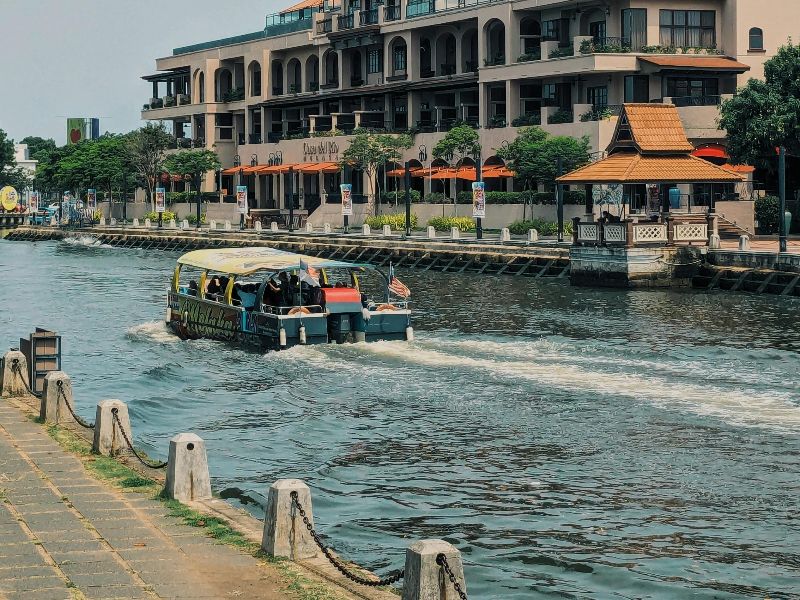 The Melaka river walkway with a boat cruising down the river