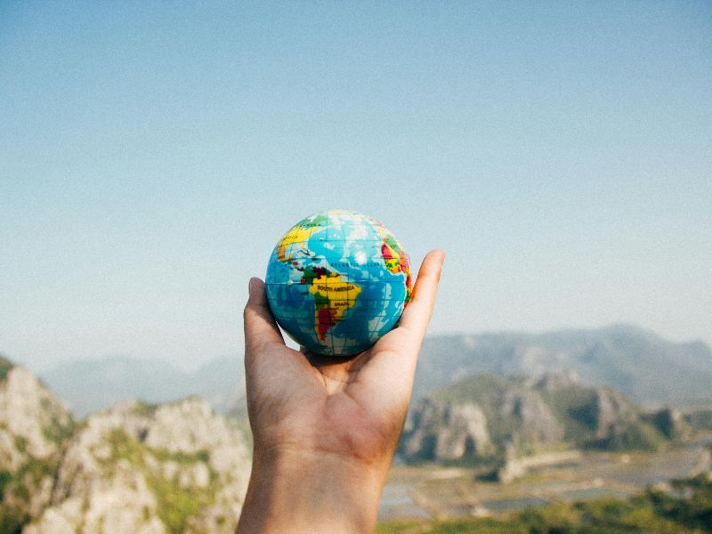 A person holding a tiny globe against scenery 