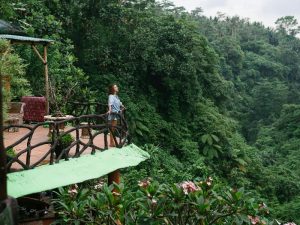 Woman stands on a cottage balcony while surrounded by a lush rainforest 